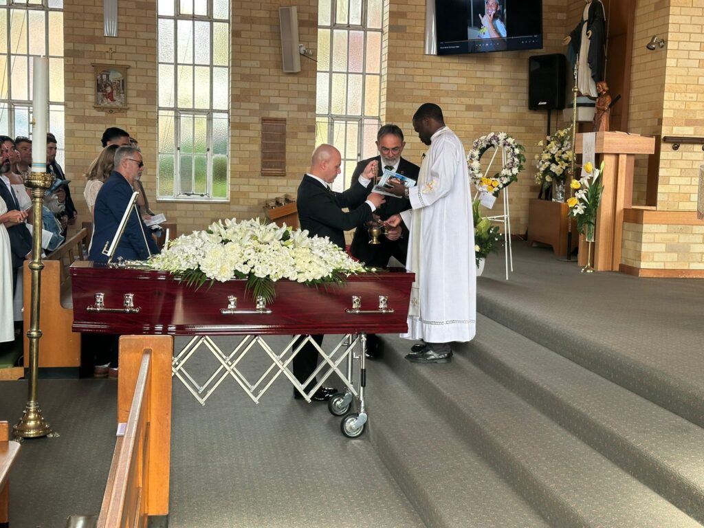 Catholic priest conducting a funeral service next to a coffin inside a Sydney church