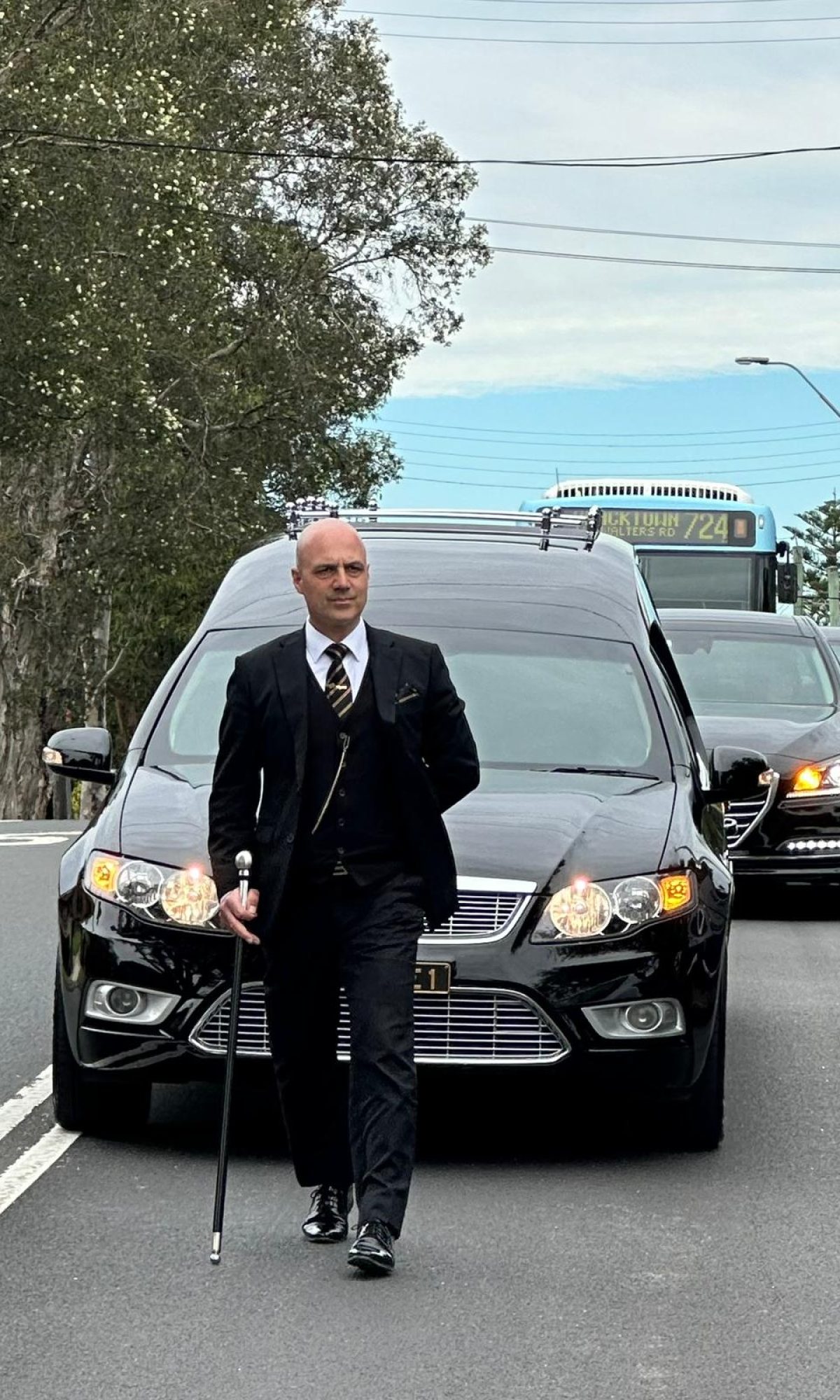 Funeral conductor leading the procession of funeral cars in Sydney.